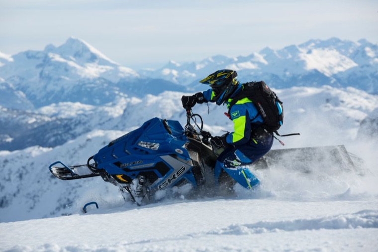 Rider carving a snowmobile across an alpine ridge