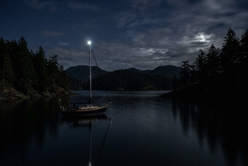 Small sailboat anchored in a dark cove at night